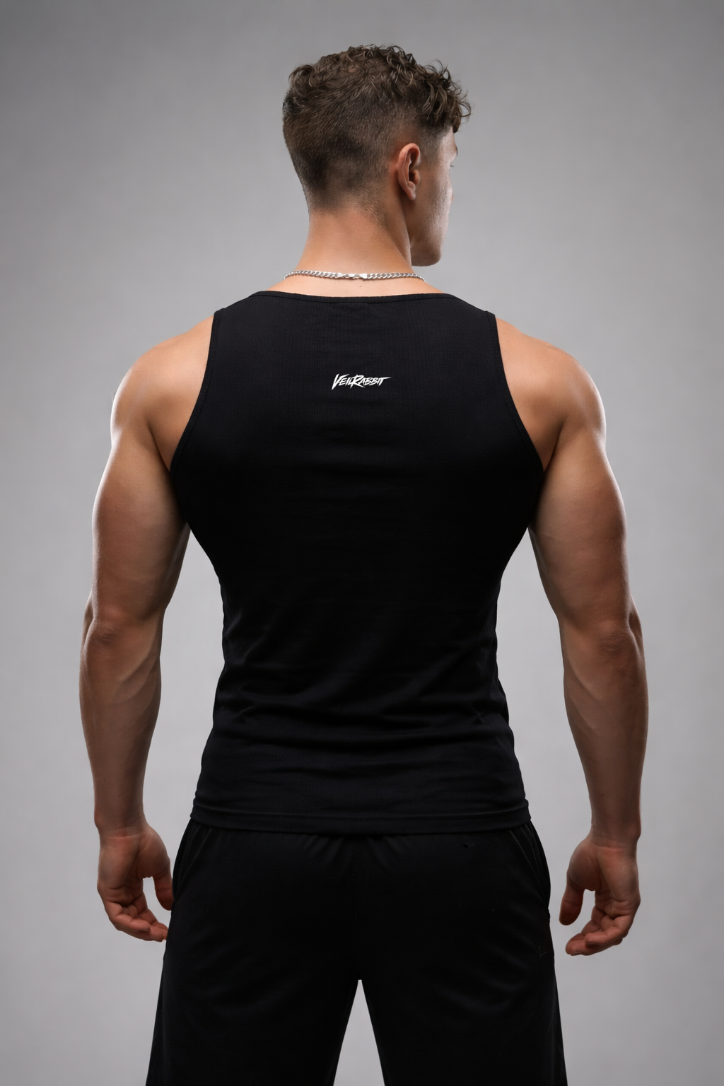 Man wearing a black tank top with a brand logo on the back against a gray background